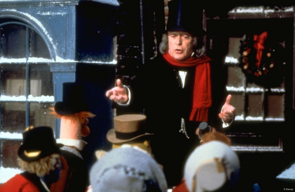 Person in top hat and red scarf is talking to puppets