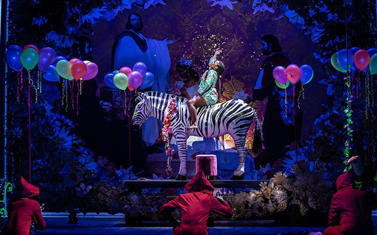 A person is sat on a zebra and there are balloons floating around them