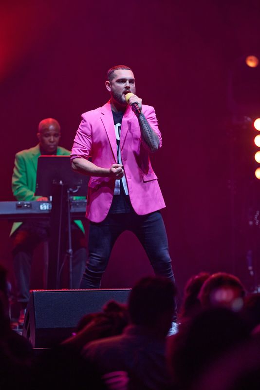 A person wearing a pink blazer sings on stage.