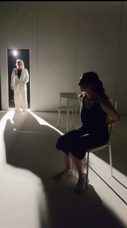 A person stood in a lit doorway and casts a shadow across the room. A person is tied to a chair