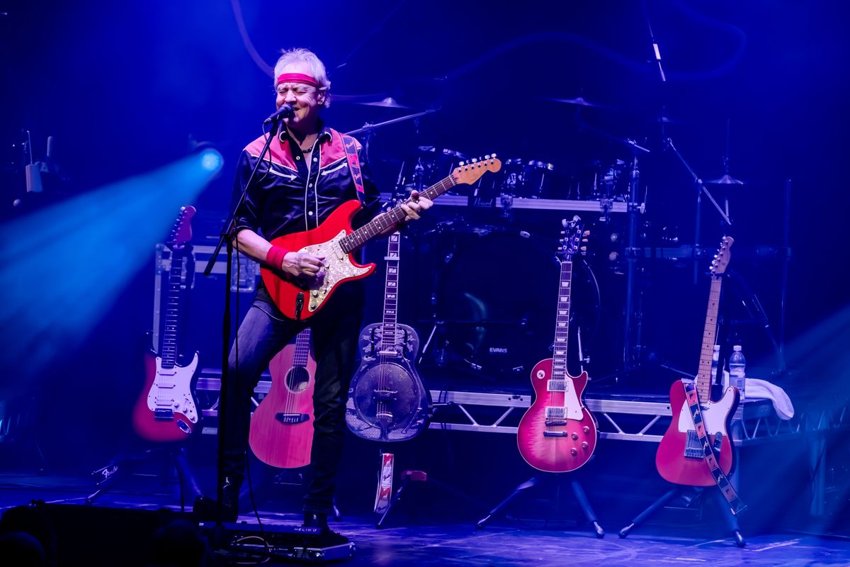 A person wearing a bandana plays electric guitar on stage.