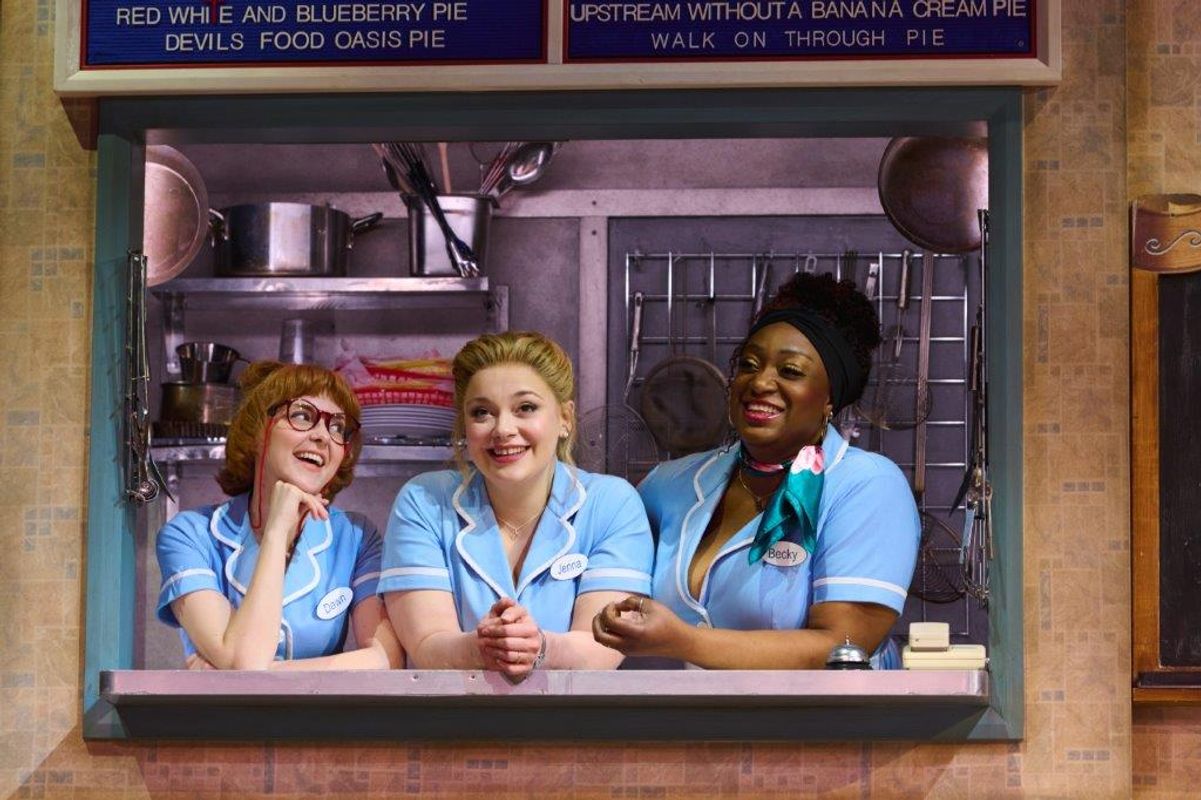 Three ladies in waitress uniform all leaning over a counter