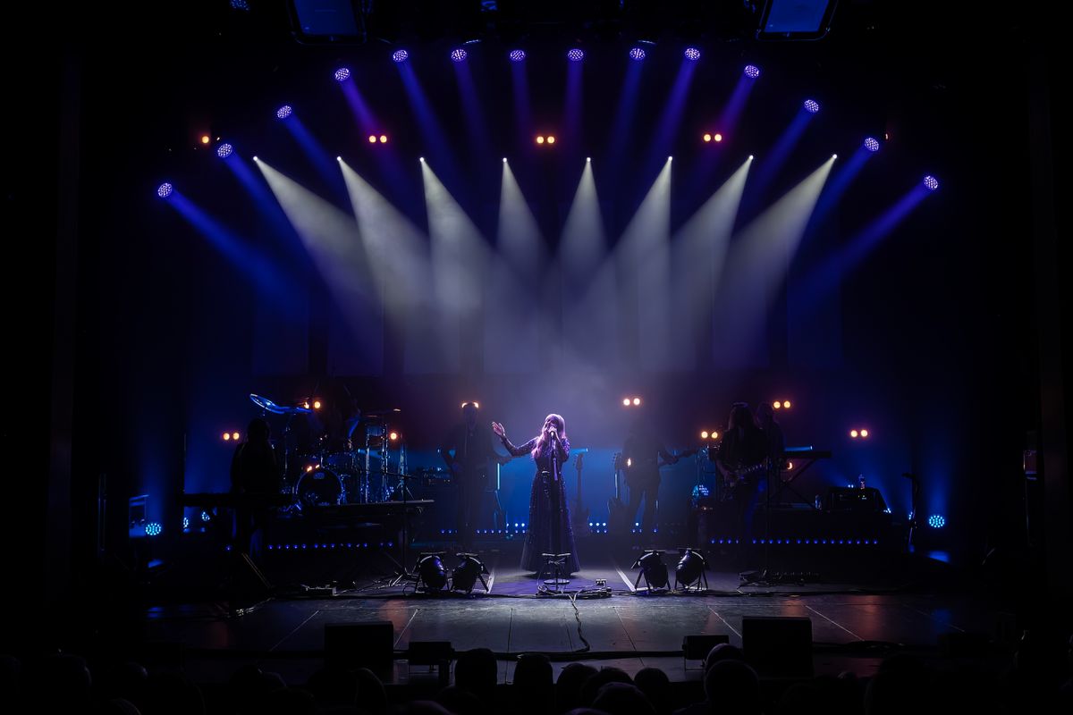 A person is lit by eight spotlights on stage.