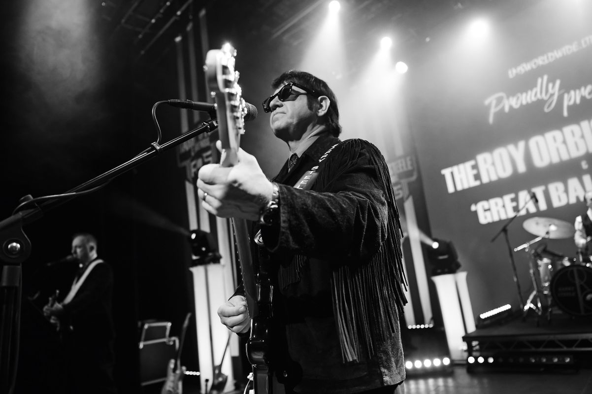 A person with a black fringed jacket plays guitar.