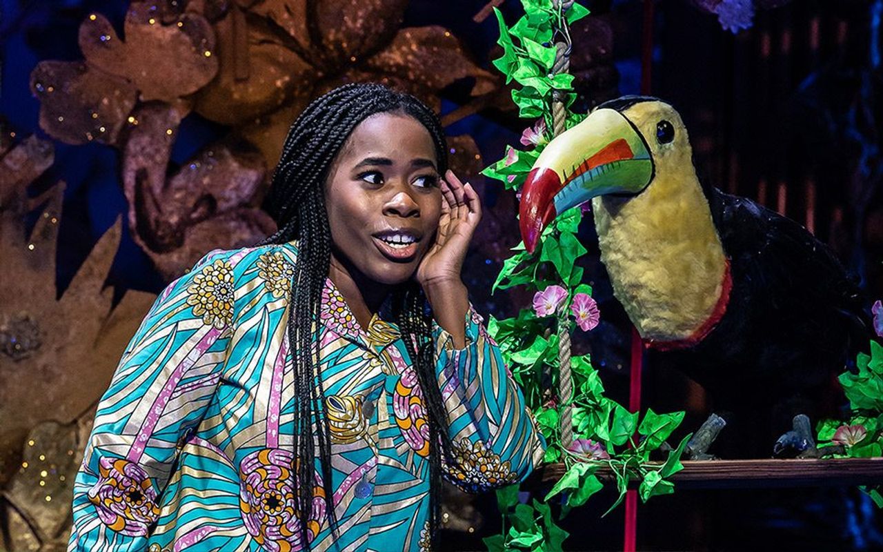 A person has their hand to their ear like they are listening to a bird they are stood next to