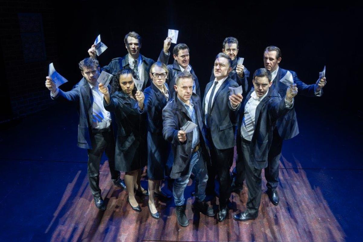 A group of people stood together and all are holding a piece if paper in the air