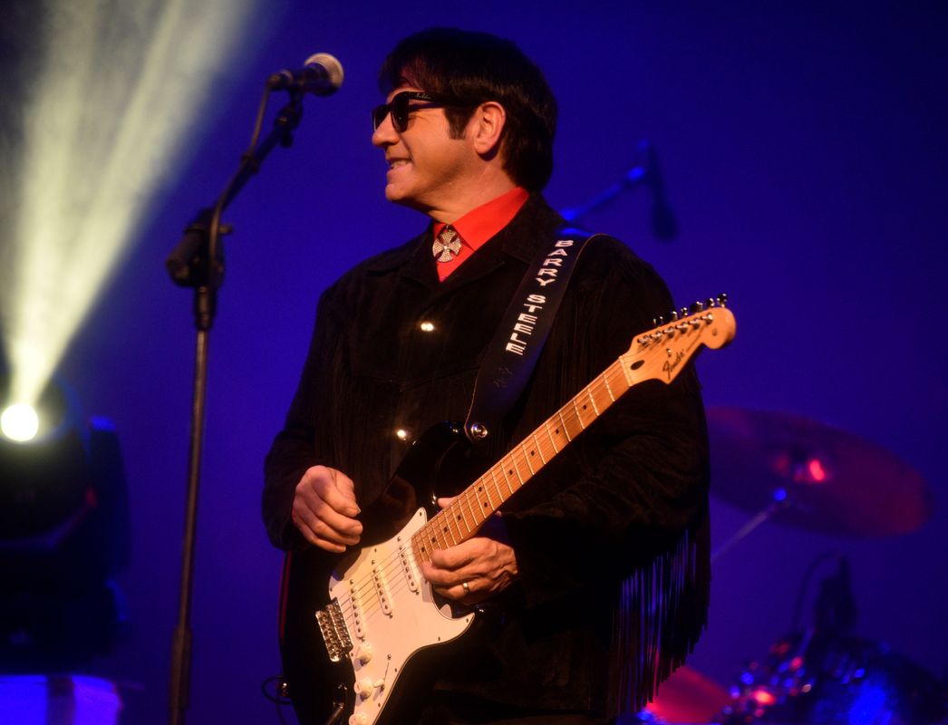 A person wearing a red shirt smiles on stage.