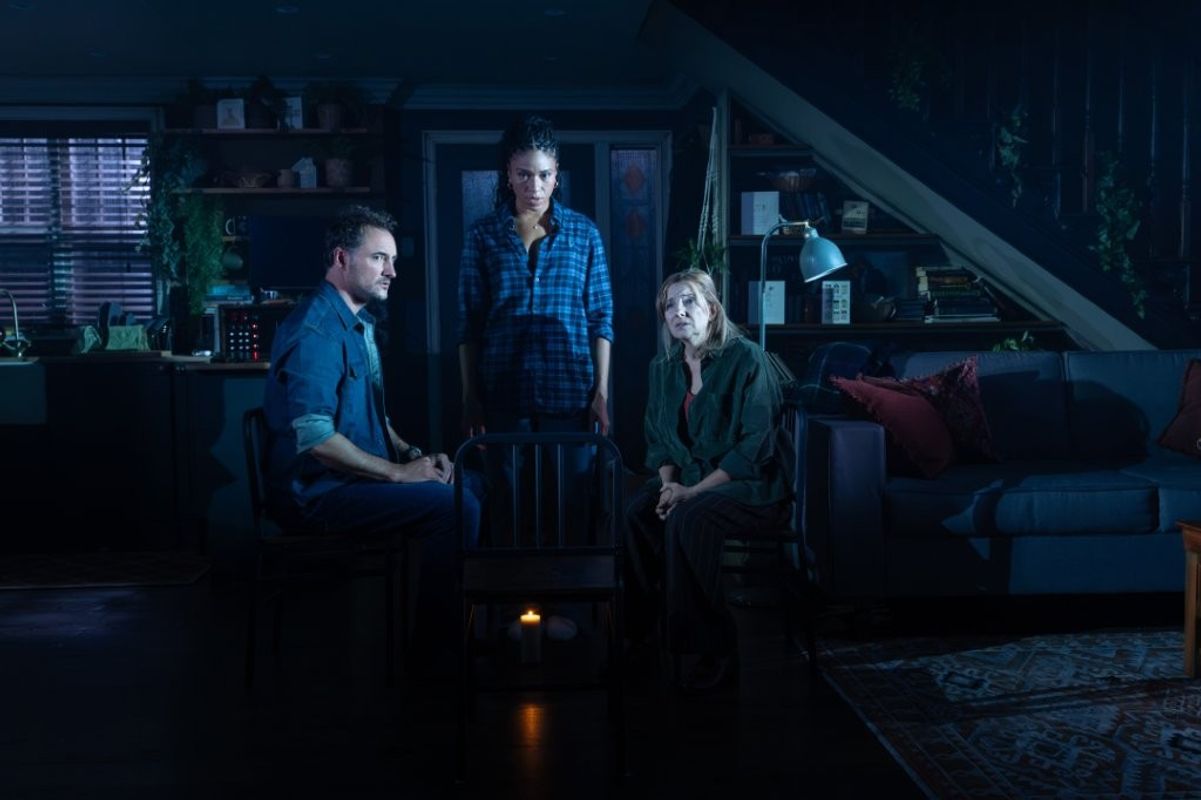 There are three people in a dimly lit room, they all look worried and concerned