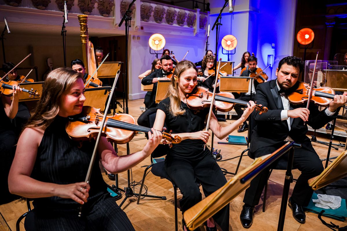 Three musicians wearing black play their violins.