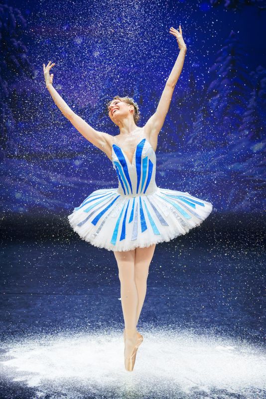 A ballet dancer stand en pointe with their arms in the air.