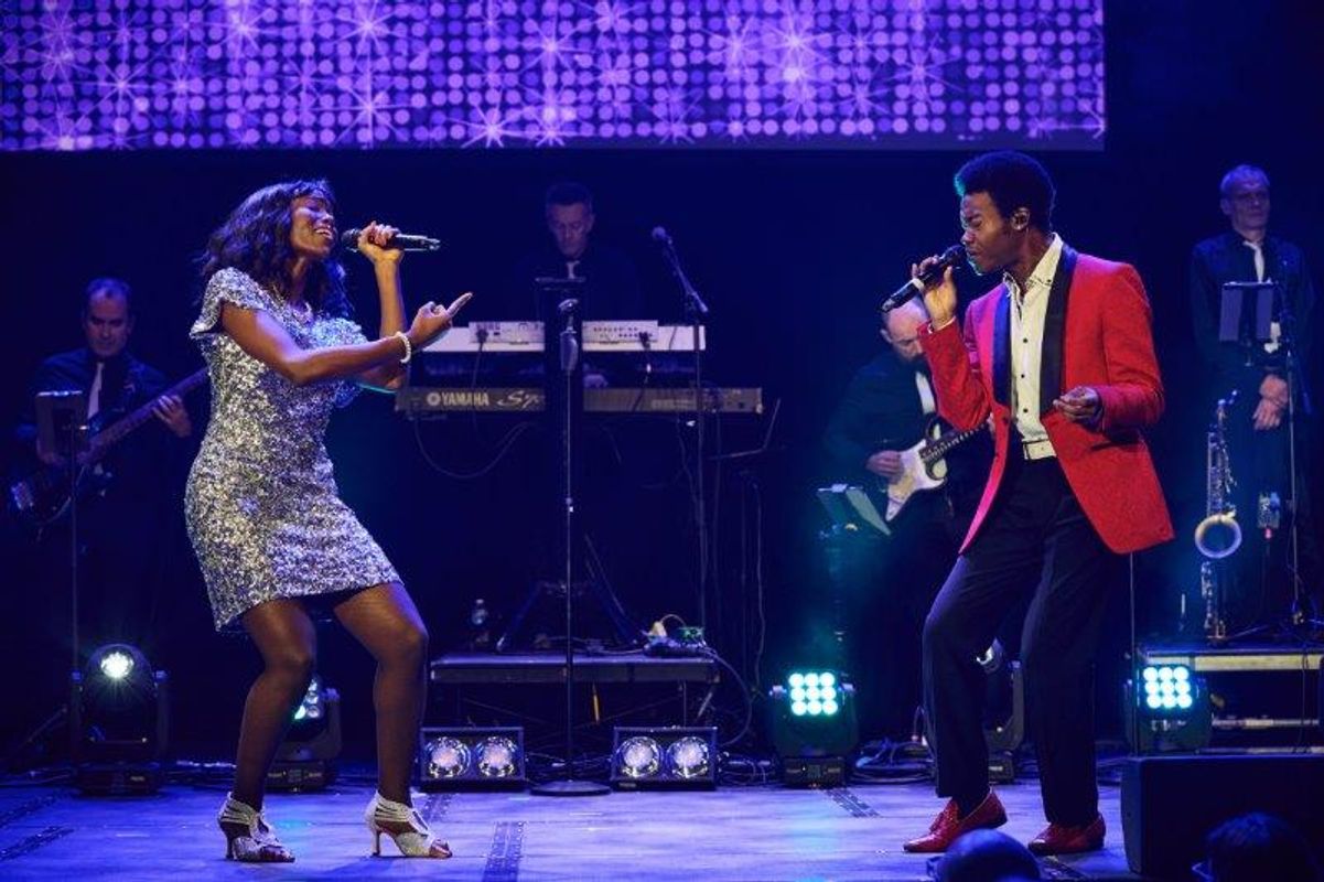 Two people stand duetting on stage.