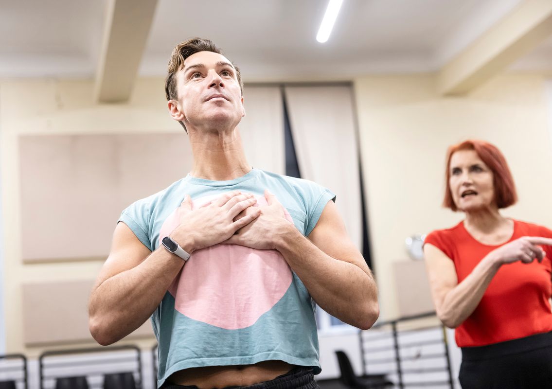 Two people, one has their hands on their chest, the other is looking towards them