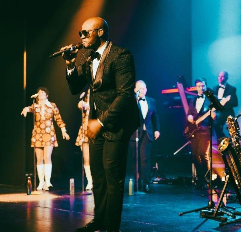 A person dressed in a suit and sunglasses sings on stage.