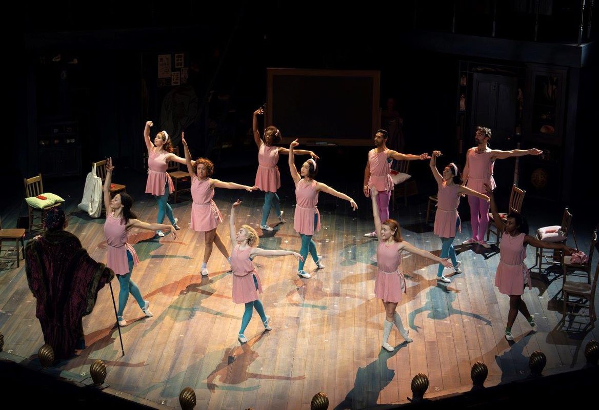Dancers are performing in front of someone. They are all wearing blue tights and pink dresses