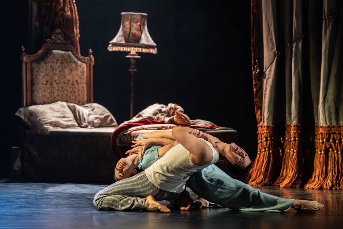 Two dancers intertwine with their backs bent.