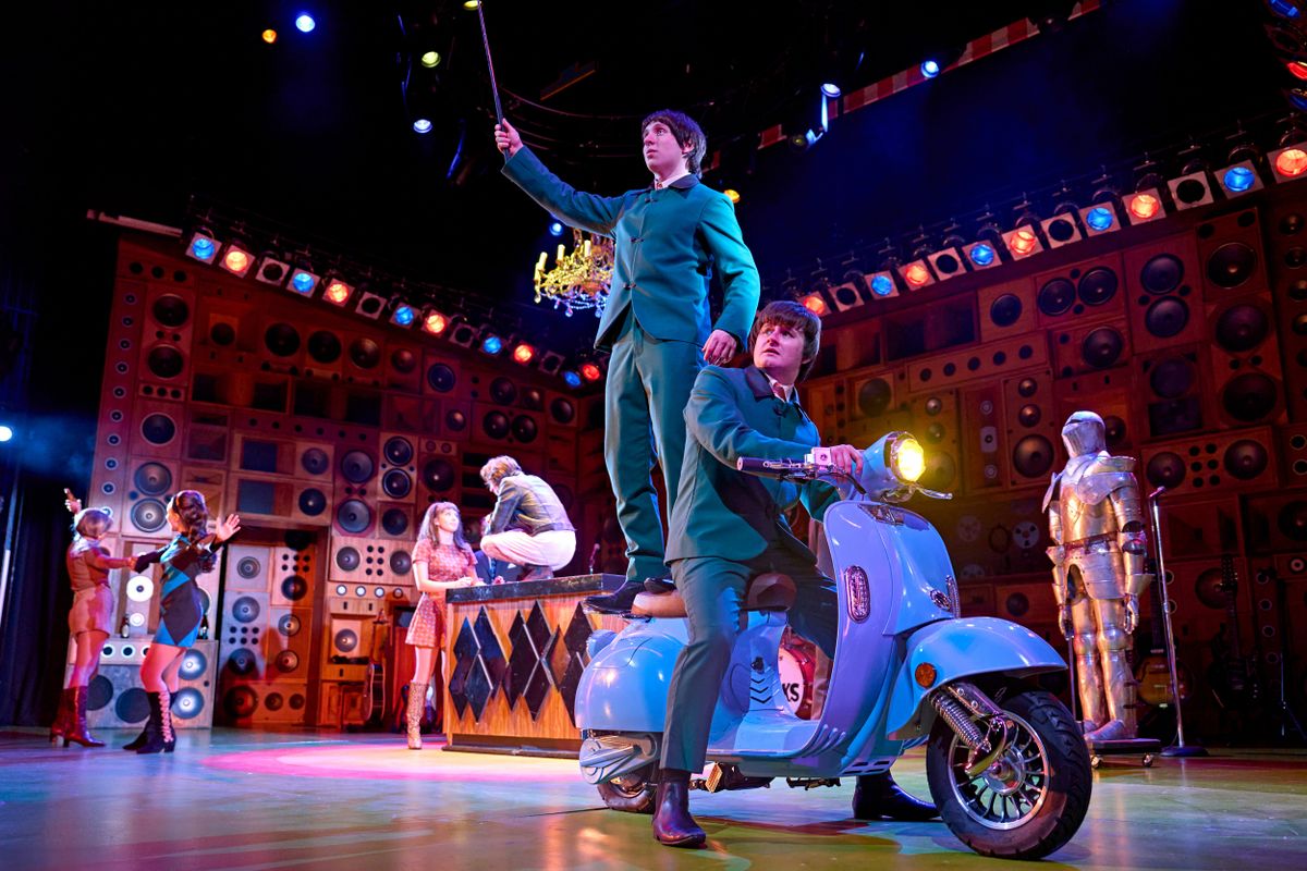 Two of the band stand and sit on a blue moped.