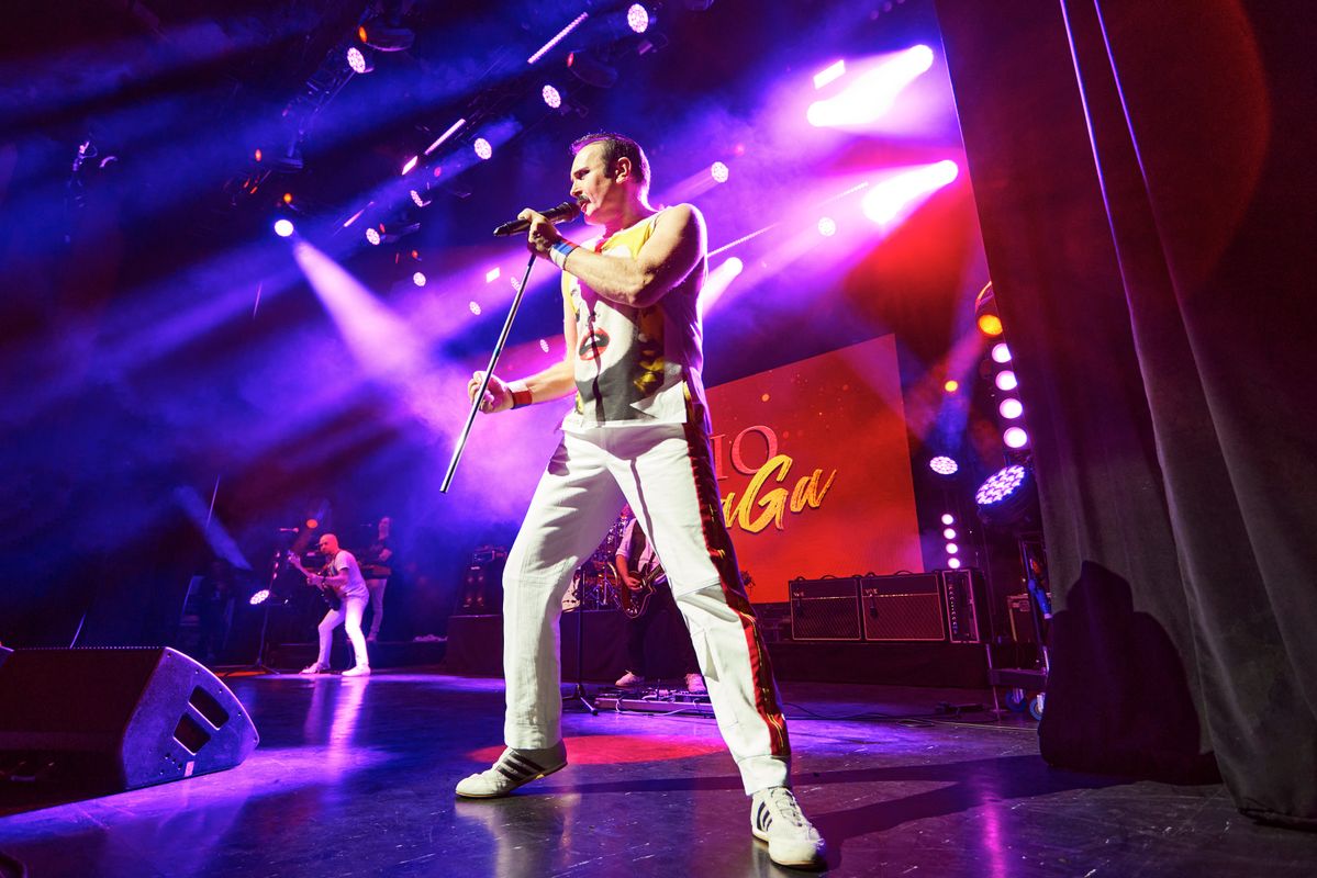 Performers singing and playing instruments on stage to an audience, bright lights are shining on the band
