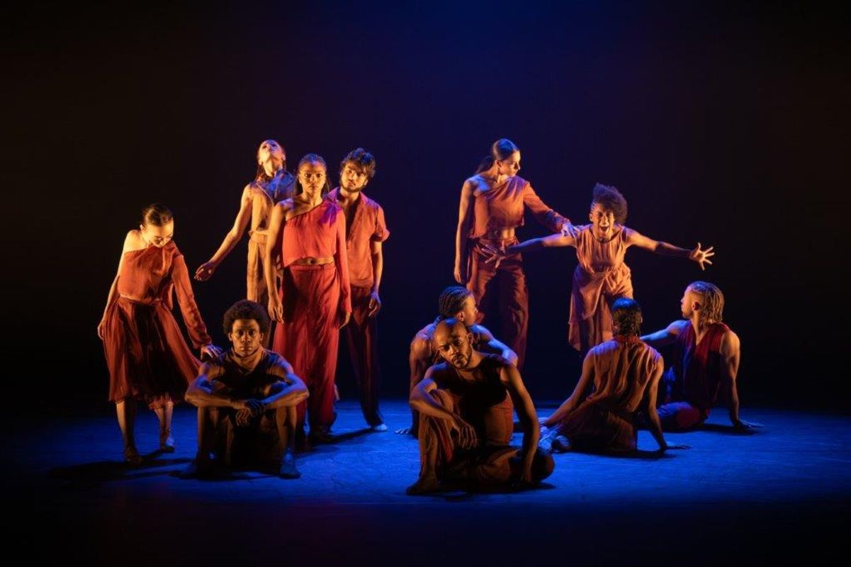 Group of dancers in orange and brown clothing with a soft spot light on them