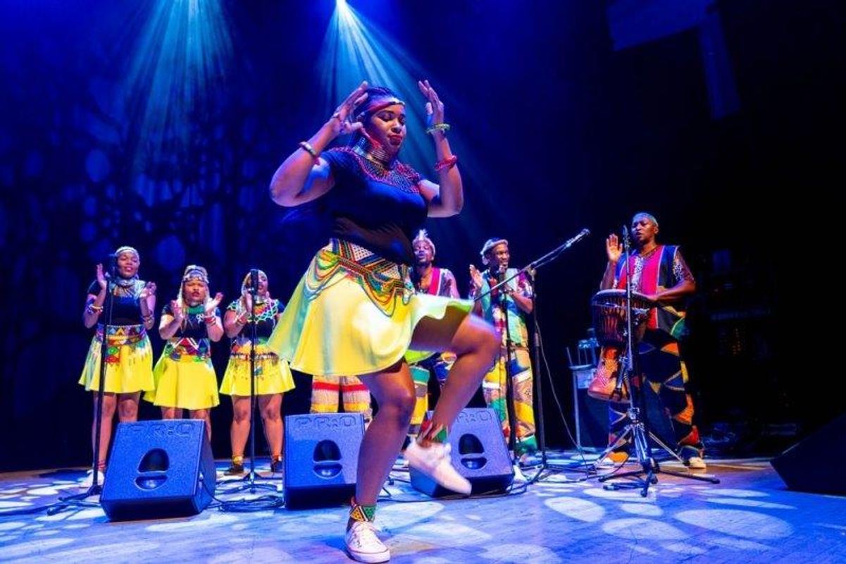 The South African Cultural Choir are singing on stage with Paul Simon. They are all wearing bright and vibrant African clothing.