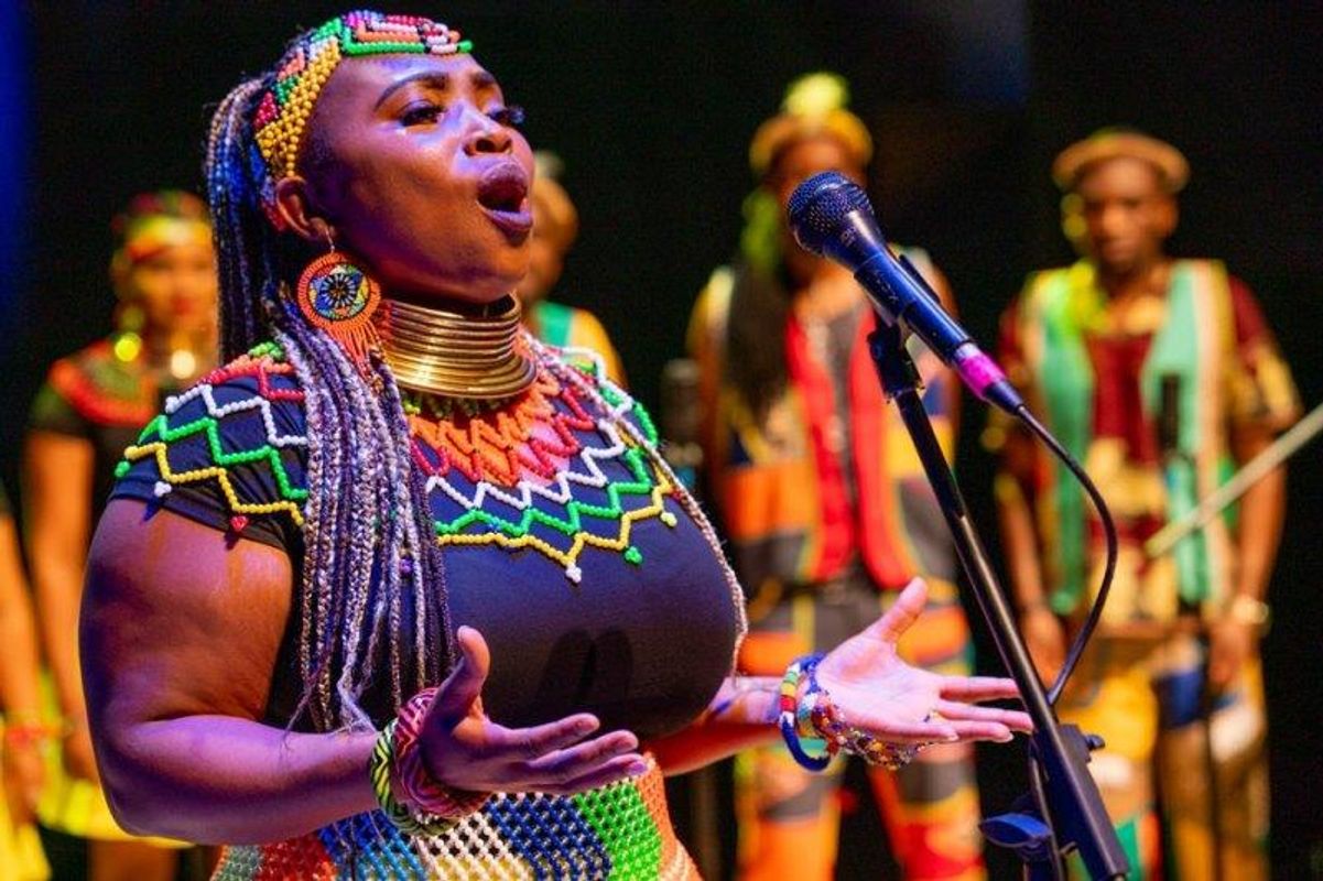 The South African Cultural Choir are singing on stage with Paul Simon. They are all wearing bright and vibrant African clothing