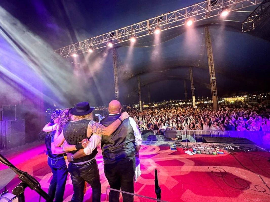The band stand looking out to the audience with their arms around each other.