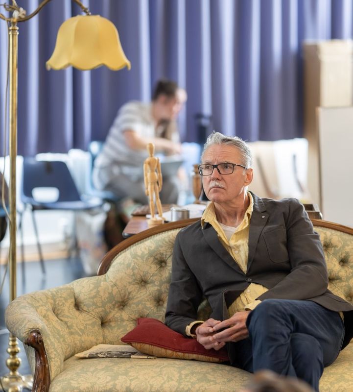 A man is sat on a sofa and there is a lamp beside him