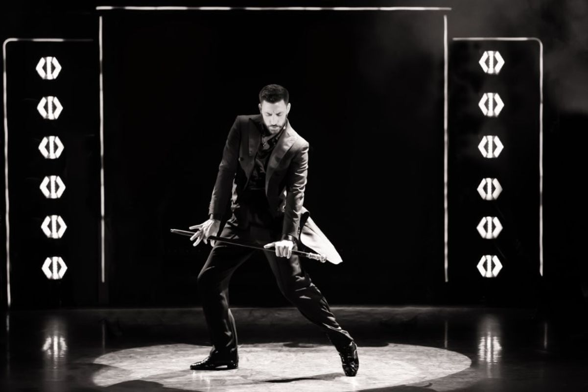 Black and white image of Giovanni dancing with a cane and is wearing a smart black suit
