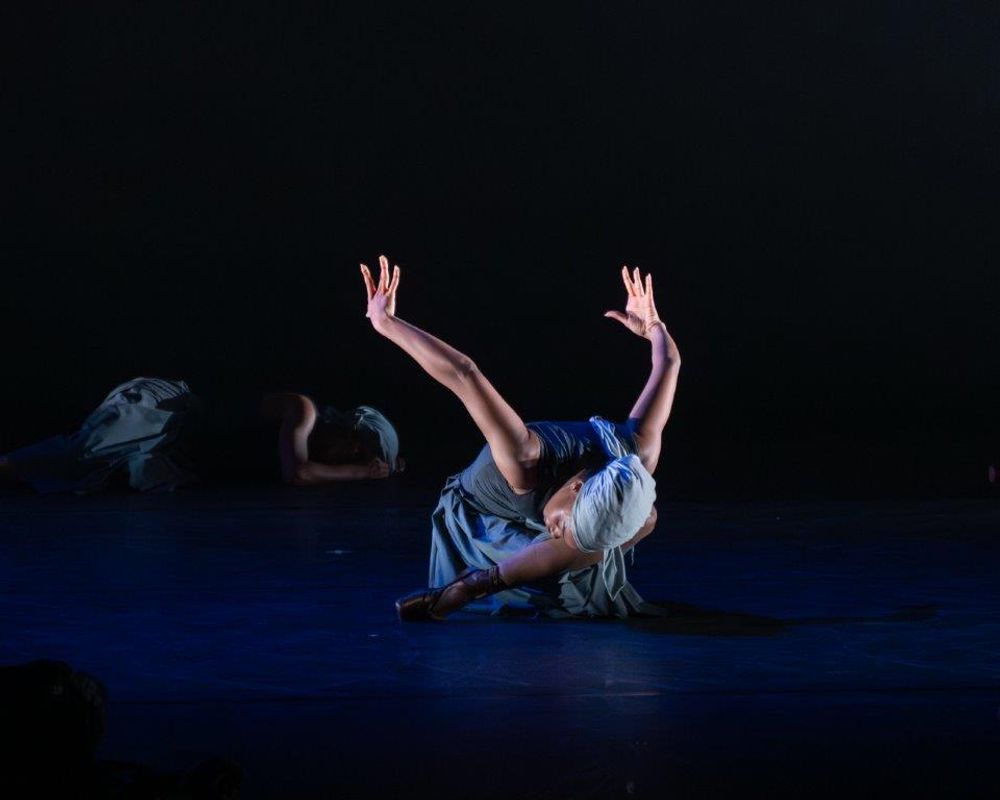 Dancer centre stage on the ground with their arms up behind them