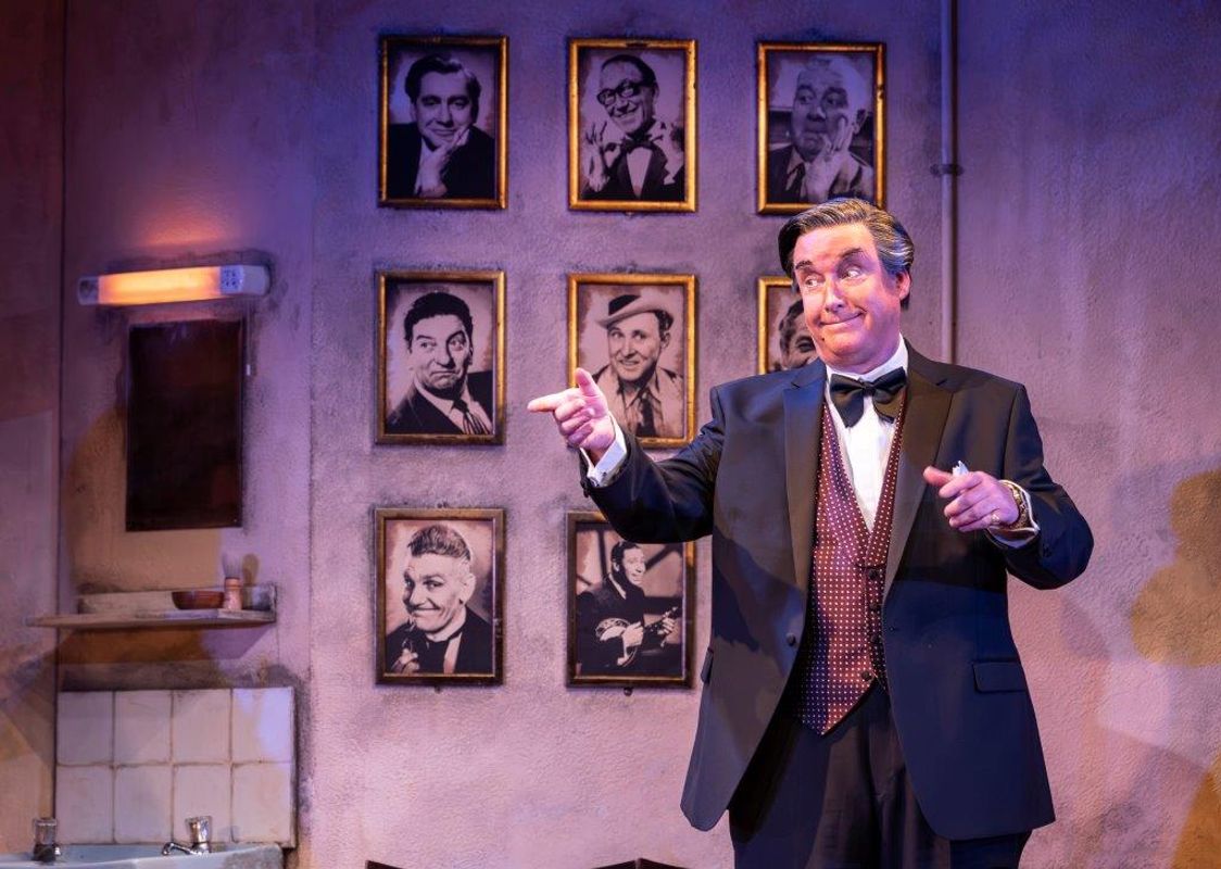 A man in  a suite, waste coat and dicky bow is pointing towards something