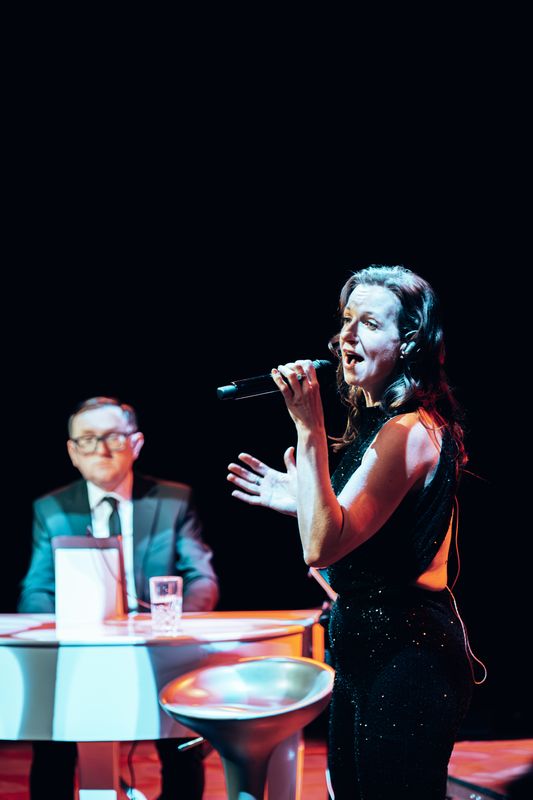 A person wearing a black sequinned jumpsuit sings.