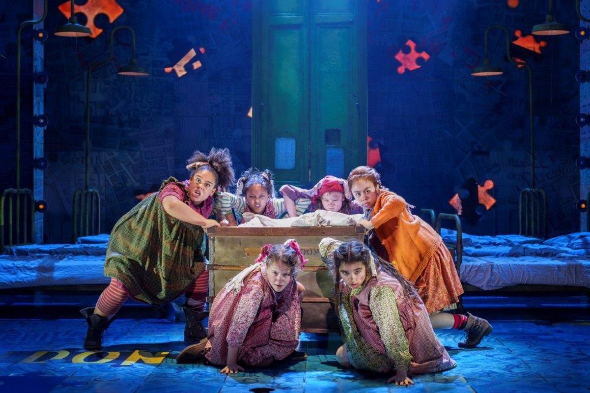 There are a group of young girls singing and dancing in a shared bedroom. They are surrounding a large trunk