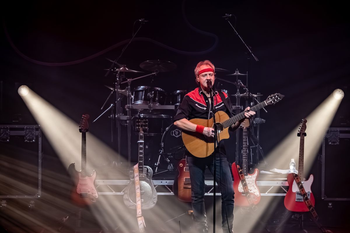 Band on stage performing, they're playing guitars and drums and there are flashing lights around them
