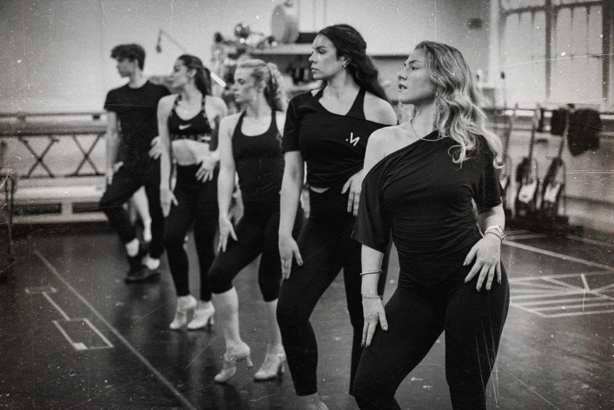 Black and white image of cats members rehearsing for Jersey boys. They are all wearing black and in a rehearsal studio