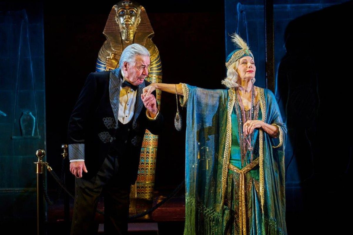 Two people stood with each other, one has their arm stretched out and the other is holding it and looks to be kissing their hand