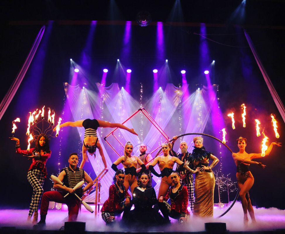 A collection of circus performers pose holding various circus apparatus. 