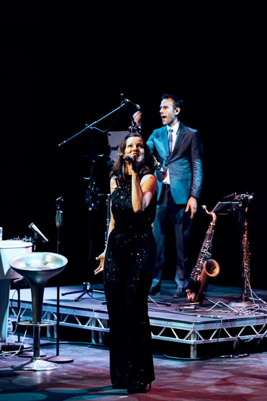 A person wearing a black sequinned jumpsuit sings.